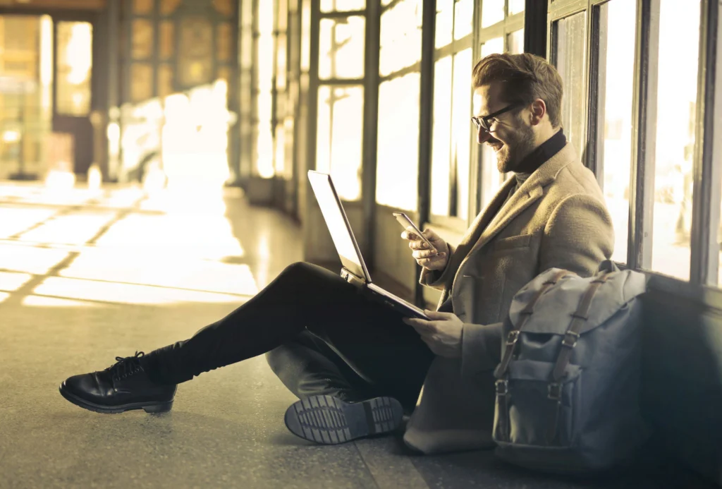 A smiling businessman checking his phone with a laptop on his knee