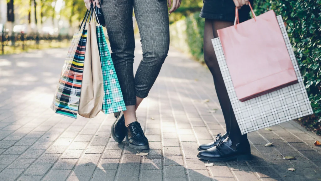Two friends carrying shopping bags along a sunny pavement