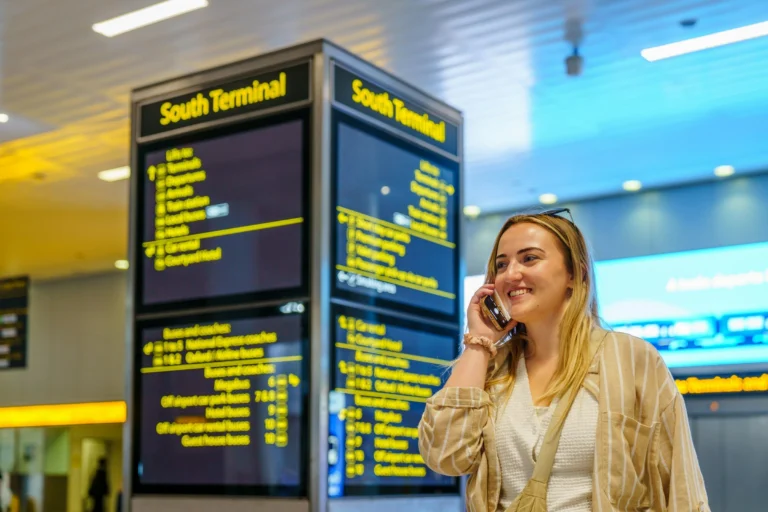 A smiling traveller on the phone beside the South Terminal information boards