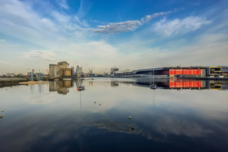 The Royal Docks and ExCeL London reflected in still water on a bright day