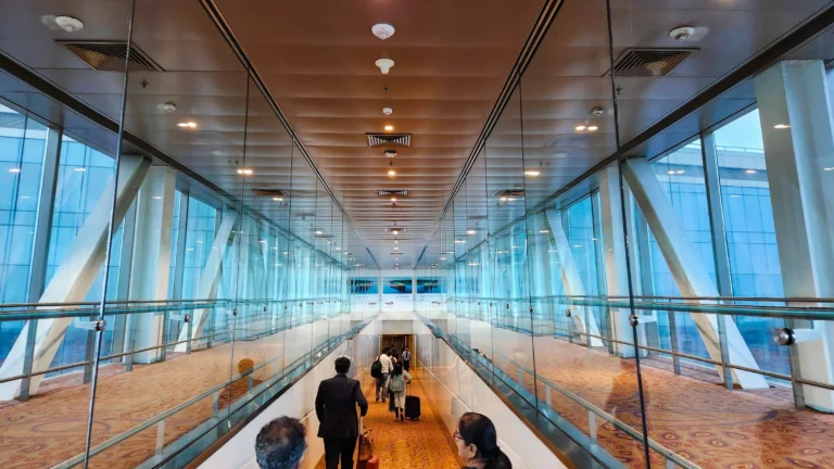 Travellers with suitcases walking along a glass-walled airport walkway