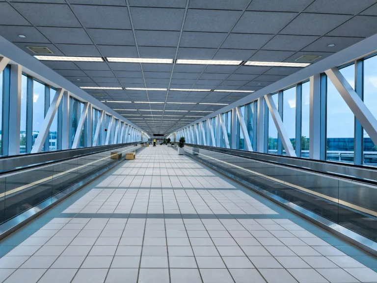 A bright, glass-walled airport walkway with moving walkways on both sides